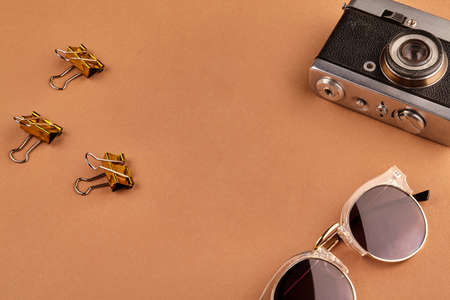 Old vintage camera, stylish sunglasses and three golden binder clips on brown studio background. Close up, copy spaceの写真素材