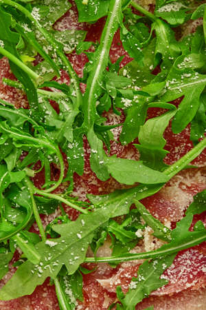 Closeup of cured ham slices with grated parmesan and arugula on pizzaの写真素材