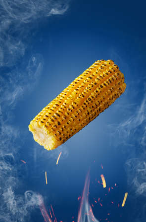 Grilled ear of corn hovering over flames in sparks and haze on blue backgroundの写真素材