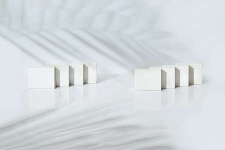 Eight small cardboard boxes isolated on white studio background. Palm tree twig shadow. Copy space,...