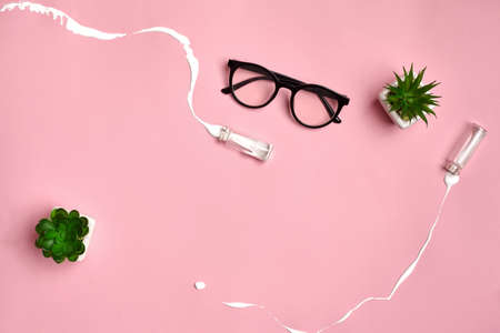 Glasses, green succulents and two small glass bottles from which spilled white liquid on pink studio background. Close up, copy spaceの写真素材