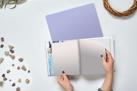 Hands of unknown woman who holding open photo book with blank pages, empty cardboard, green twig and...