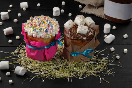 Two Easter cakes with whipped egg whites and chocolate icing with marshmallows on hay
