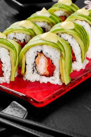 Closeup of uramaki rolls with shrimp, tobiko, avocado and mayonnaise on red plateの写真素材