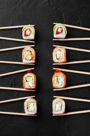 Various sushi rolls with salmon, eel, shrimp, avocado and caviar in chopsticks on black surfaceの写真素材