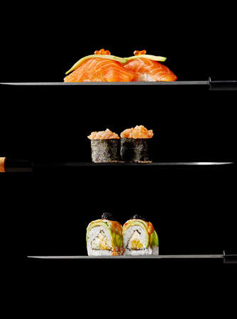 Nigiri sushi with salmon, gunkan maki and uramaki with avocado and shrimp on knife blades on black...