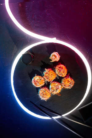 Sushi rolls with melted cheese and bonito flakes on black background with LED strip lighting