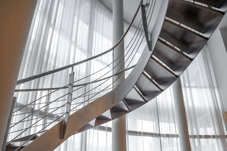 Spiral staircase in mansion on background of wide window covered with white curtainsの写真素材