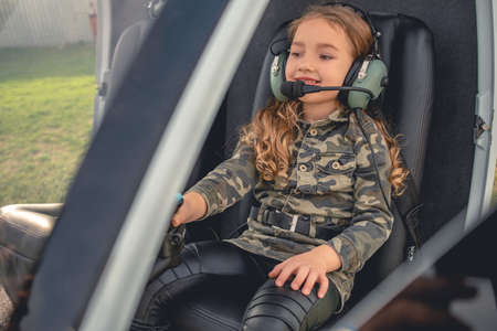 Cheerful tween girl in headset sitting on pilot seat in helicopterの写真素材
