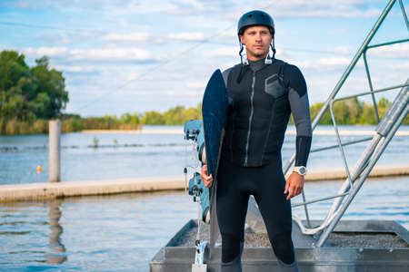 Confident wakeboarder standing on pier with board in hand