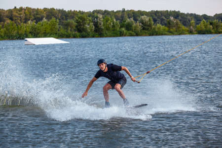 Man balancing on wakeboard towed on cable trying to make grab of boardの写真素材