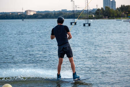 Back view of sporty man balancing on wakeboard, riding on city riverの写真素材
