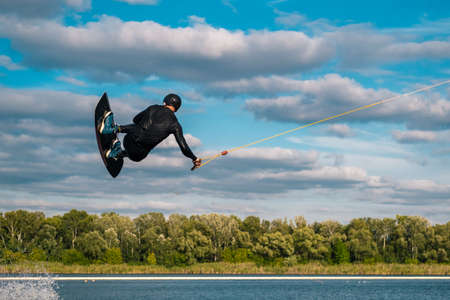 Experienced wakeboard rider towed on cable jumping and spinning in air in open waterの写真素材