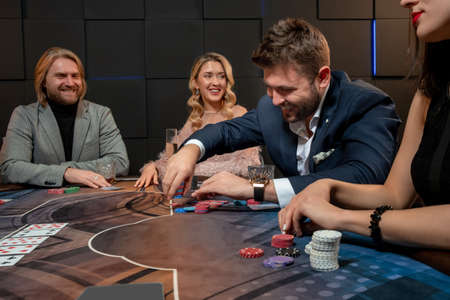 Cheerful bearded guy sitting at poker table in casino and making bet