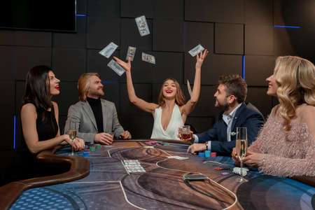 Cheerful girl winning poker tossing banknotes into air at gaming table