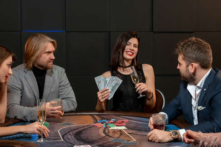 Cheerful young brunette with banknotes and glass of champagne at poker table