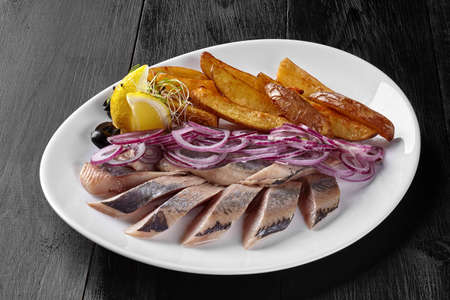 Salted herring with fried potato wedges, onion and lemonの写真素材