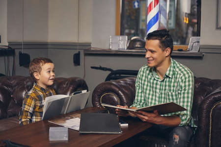 Young father and his stylish little son in the barbershop in the waiting room.