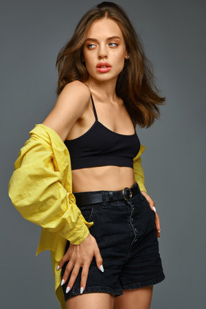 Girl in black shorts and yellow shirt posing on grey backgroundの写真素材