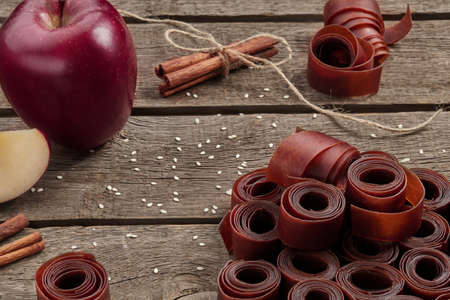 Rolls of fruit leather on wooden surface with apple and cinnamon