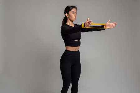 Girl doing arm and shoulder exercises with resistance band on grey background