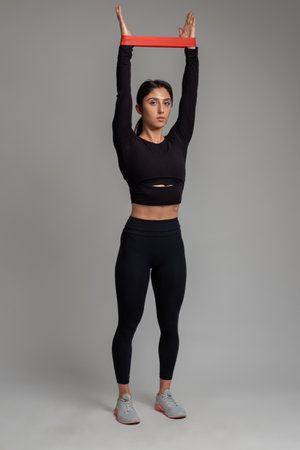 Girl performing upper body workout with resistance band on grey background