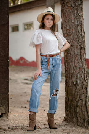 Stylish confident teenage girl standing near tall pine tree in country estate in summerの写真素材