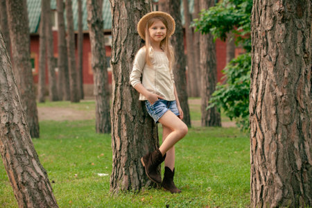 Smiling tween girl leaning against tall tree in courtyard of country house in summerの写真素材