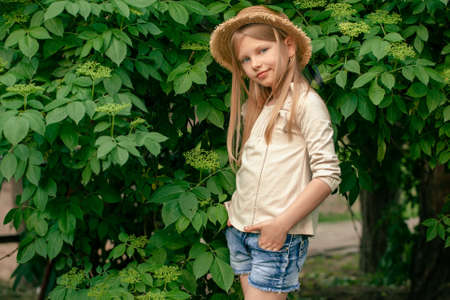 Smiling tween girl standing near green elderberry bush in summer gardenの写真素材