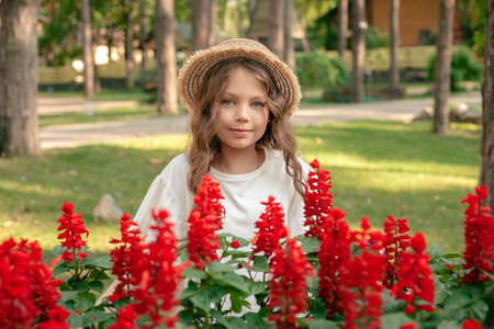 Smiling preteen girl posing next to blooming red flowers at country estateの写真素材