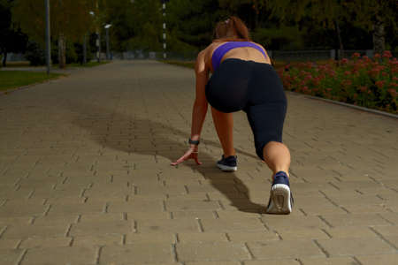 Girl athlete stretching in morning outside, in the city, on a park path surrounded by trees. Active...