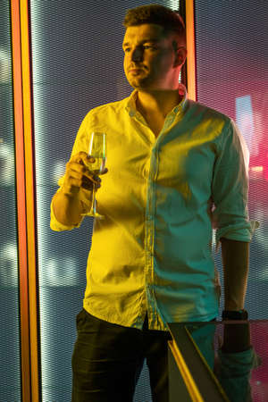 Relaxed man standing with glass of wine in colored nightclub lightingの写真素材
