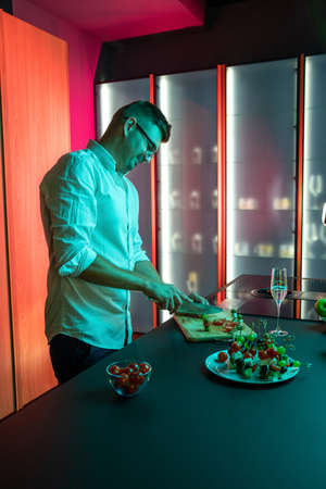 Smiling young man preparing snacks for romantic dinner in home kitchenの写真素材