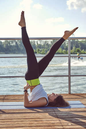 Woman in white undershirt and black leggings is practicing yoga performing yoga-asanas on a mat...