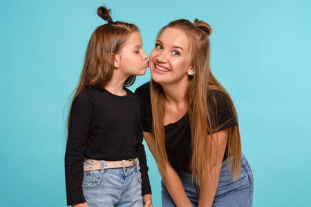 Mom and daughter with a funny hairstyles, dressed in black shirts and blue denim jeans are posing...