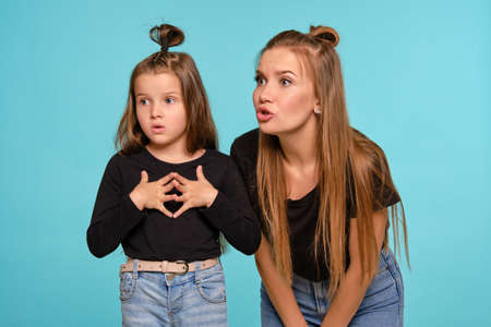 Mom and daughter with a funny hairstyles, dressed in black shirts and blue denim jeans are posing...