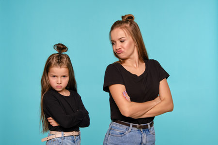 Mom and daughter with a funny hairstyles, dressed in black shirts and blue denim jeans are posing...