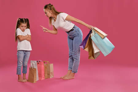 Mom and daughter with ponytails, dressed in white t-shirts and blue jeans are posing against pink...