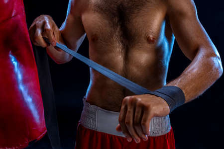 Boxer preparing her gloves for a fight. Photo of muscular man strapping up hands on black...