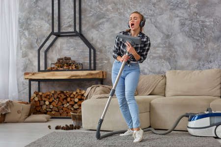 Cheerful young woman enjoying solo singing with vacuum cleaner while cleaning houseの写真素材