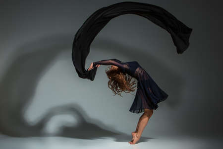 Young beautiful dancer in black dress posing on a dark gray studio backgroundの写真素材