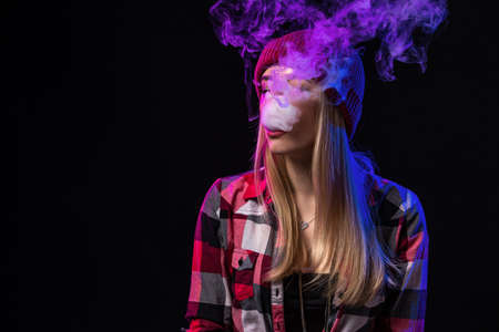 Vaping girl. Young hipster woman vape e-cig on studio on black background. Hip-hop style. Close up.の写真素材