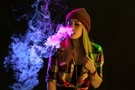 Vaping girl. Young hipster woman vape e-cig on studio on black background. Hip-hop style. Close up.の写真素材