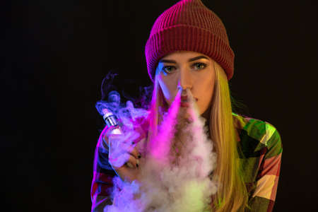 Vaping girl. Young hipster woman vape e-cig on studio on black background. Hip-hop style. Close up.の写真素材