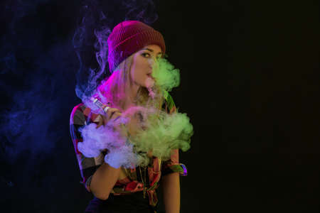Vaping girl. Young hipster woman vape e-cig on black background. Hip-hop style. Studio shotの写真素材