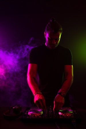 Attractive young DJ playing on turntables with color light effectsの写真素材