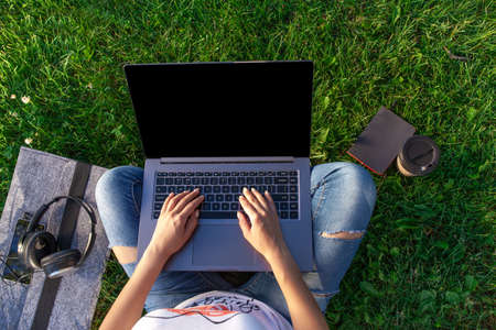 Top view. Woman working on laptop pc computer with blank black empty screen to copy space in park on green grass sunshine lawn outdoors.の写真素材