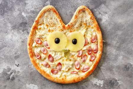 Owl-shaped pizza for kids with cream cheese sauce, chicken, Vienna sausage, pineapple, olives, pickled cucumber and sesameの写真素材