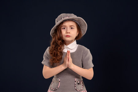 Studio shot of a lovely little kid with a long, curly hair posing on a black background.