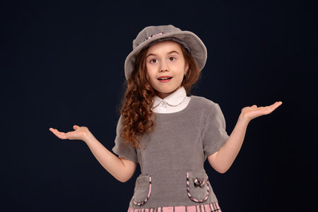Studio shot of a lovely little kid with a long, curly hair posing on a black background.